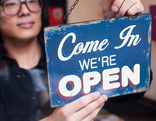 A person in a doorway of a business changing a sign that reads "Come In We're Open"